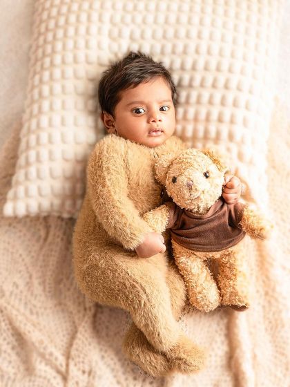 This little teddy is wide awake and holding his own tiny bear. The neutral colors and soft textures are perfect for a warm and gentle newborn photoshoot.