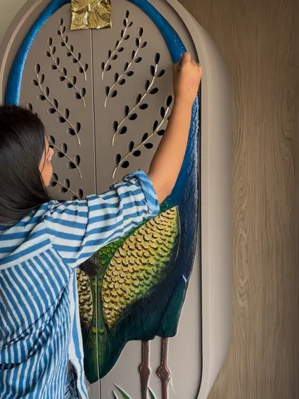A close-up of me working on a custom art piece for a wardrobe shutter, featuring a painted peacock with gold leaf details. This shows how I can integrate art into bespoke furniture design.