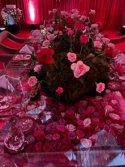 A detailed view of the tablescape, where a carpet of red and pink rose petals on a mirrored surface reflects the towering centerpiece of moss and fresh roses. This creates an illusion of infinite florals.