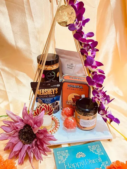 An elegant and modern Diwali hamper. This triangular stand holds premium goodies like Hershey's exotic darks, chaka shaka chai, and is decorated with orchids and a diya.