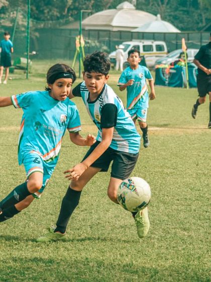 A player shields the ball from a defender near the corner flag, trying to maintain possession.