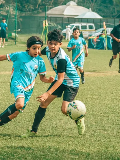 A player shields the ball from a defender near the corner flag, trying to maintain possession.
