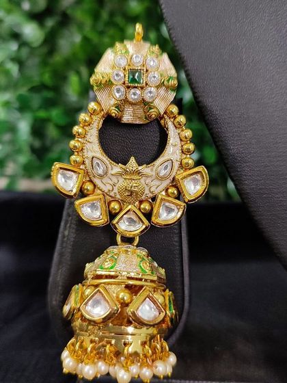 A detailed view of an earring from a for-sale bridal set. The piece showcases beautiful white enamel work with green accents and a classic jhumka design.