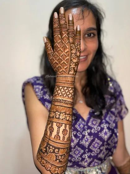 A smiling bride showing off her beautiful back-of-hand mehendi. The design is a perfect blend of traditional patterns and modern elegance.