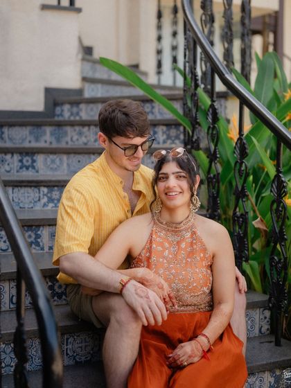 A relaxed and intimate portrait of a couple sitting on a staircase in Goa. This photo captures the casual, unfiltered vibe of a destination wedding, focusing on the genuine connection between two people from different cultures.