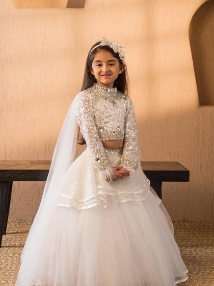 An angelic white lehenga with a fully sequined, high neck blouse and a layered tulle skirt. The attached dupatta adds a touch of grace.