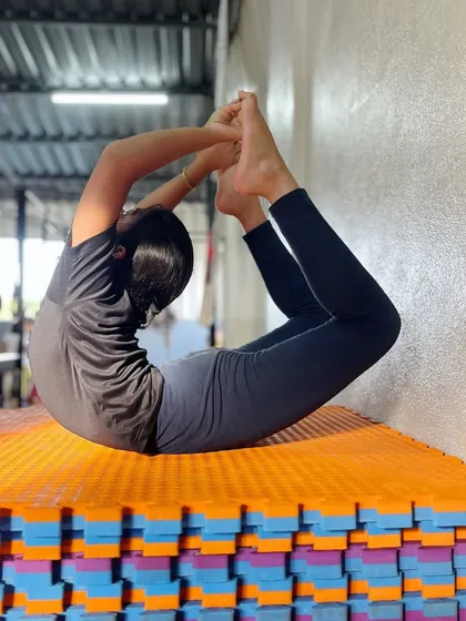 A perfect bow pose, or Dhanurasana, against the wall for support. We use various techniques to help students deepen their stretches and improve their back flexibility.
