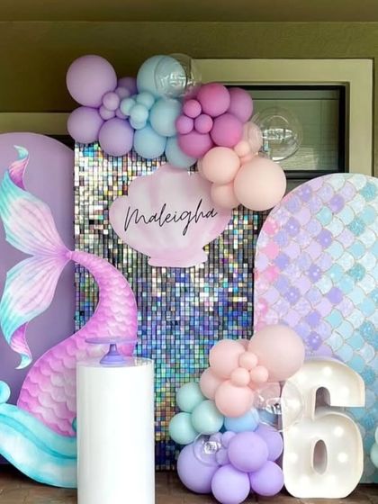 A mermaid-themed 6th birthday party with a beautiful iridescent mermaid tail, a shimmer wall, and a marquee number "6". The pastel balloon colors complete the under-the-sea look.