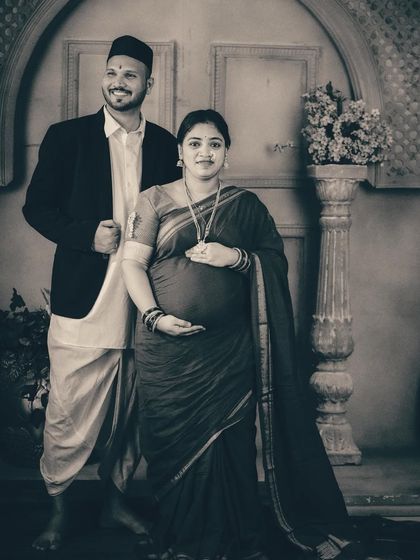 A formal couple's portrait in black and white, emphasizing their proud stance and traditional clothing. The lack of color adds a sense of history and permanence to this Maharashtrian-themed maternity photo.