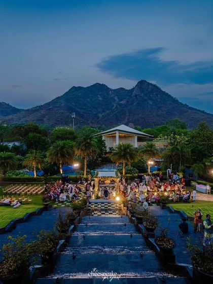A wide shot showing the scale of a destination wedding in Udaipur, with the ceremony set against a mountain backdrop at dusk.