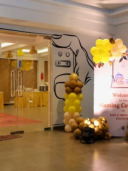 We make sure your guests feel the celebration from the moment they arrive. This entrance decor for a naming ceremony features a personalized welcome sign framed by a beautiful balloon arch in shades of yellow and brown.