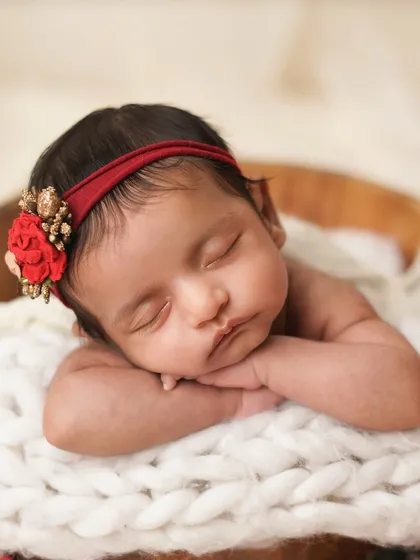 A detailed close-up of the newborn's face, showing her delicate features and the beautiful red floral headband that complements the theme.
