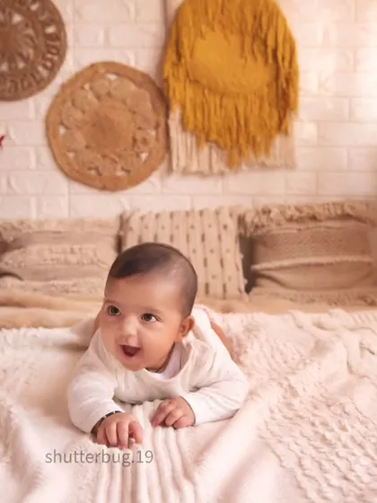 A wide shot of a happy baby during tummy time on a soft blanket. This photo is part of a larger family session that includes both individual shots of the baby and group portraits.