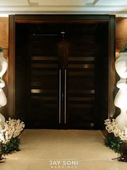 A modern and clean entrance design, where minimalist white totems and simple green arrangements create a path leading to the main event space.