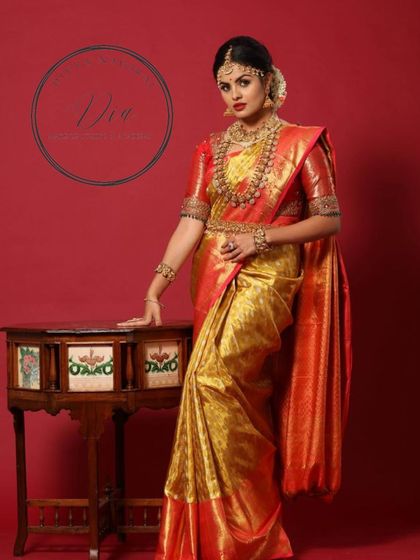 A full-length portrait of a model in a stunning red and gold Kanjeevaram saree. The makeup is classic bridal glam, with bold eyes and lips, paired with heavy temple jewellery for a majestic look.
