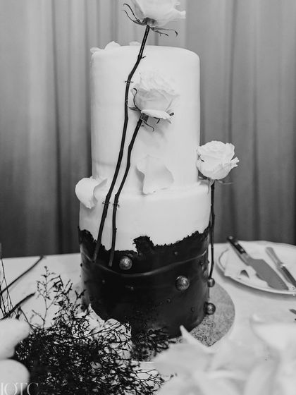 A stunning black and white wedding cake, adorned with delicate white roses and black branches, perfectly matching the theme.