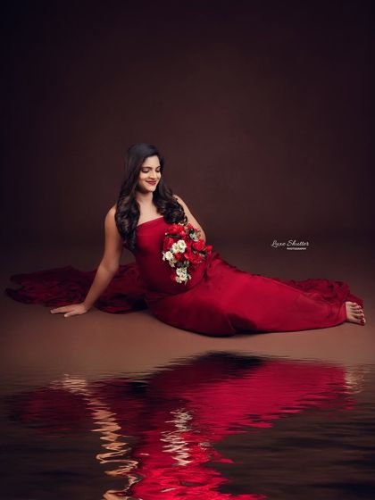 A seated portrait with a water reflection, creating a moody and artistic image. The red gown pops against the dark background.