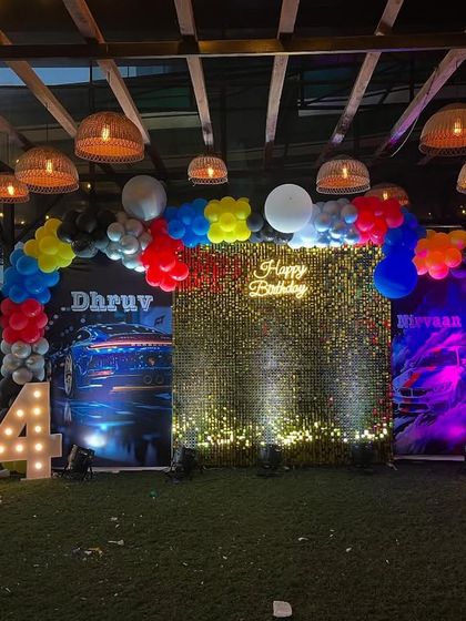 A joint birthday celebration with a cool car theme. The setup features a grass-like floor, a shimmer wall, custom car backdrops, and large marquee numbers for each birthday boy.