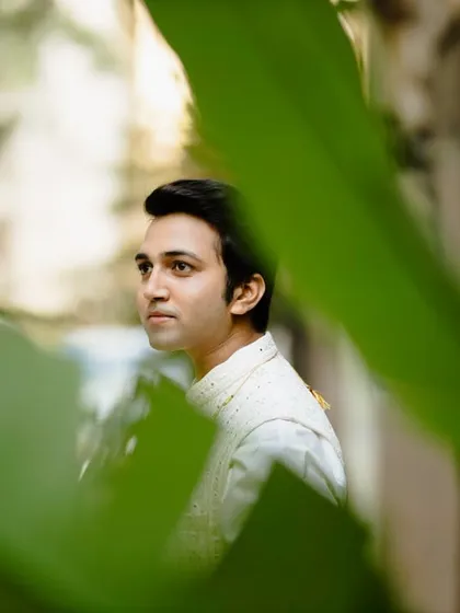 A handsome portrait of the groom, framed by lush green leaves. The natural setting and his thoughtful expression create a serene and stylish image.