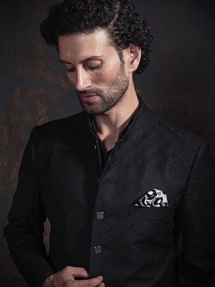 A close-up of a black Indo-Western jacket with a subtle checkered texture. Paired with a patterned pocket square, it’s a look that speaks of quiet confidence and attention to detail.
