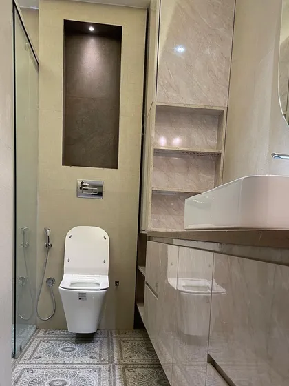 A full view of the bathroom with patterned tiles, showing the wall-mounted toilet and the built-in storage niche with accent lighting.