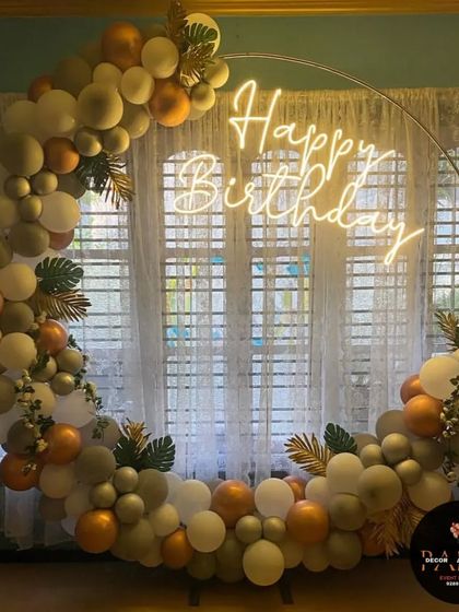 An elegant ring decoration with muted green, gold, and white balloons, accented with artificial leaves for a touch of nature.