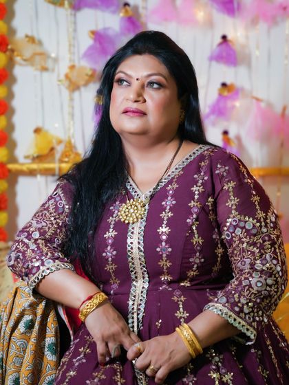 A pretty and dramatic look for a festive event. The makeup is glamorous, with a focus on the eyes, and complements her embroidered purple outfit.