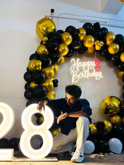 A fun shot of a 28th birthday celebration with a black and gold balloon arch and light-up numbers.