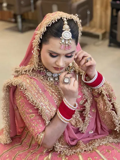 A Punjabi bride in a beautiful dusty pink lehenga. This candid shot captures the intricate details of her jewelry and the soft, smoky eye makeup that gives her a royal and elegant feel.
