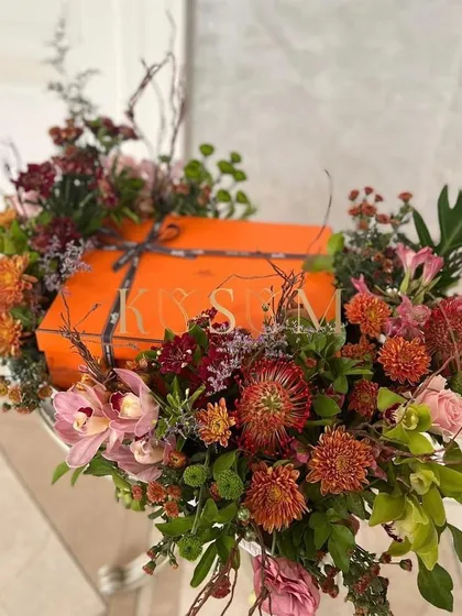 I love matching the floral design to the gift itself. Here, a luxury gift box is enveloped in a rich, autumnal palette of pincushion proteas, cymbidium orchids, and deep red chrysanthemums, creating a cohesive and artistic presentation.