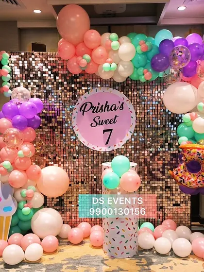 This "Sweet 7" candy-themed party shows how I use color and texture. The backdrop is a shimmering rose gold sequin wall, framed by a pastel balloon garland with fun elements like a donut and ice cream cone, perfect for a vibrant celebration.