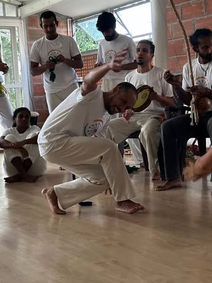 An instructor leads the game in the roda, playing the pandeiro (tambourine) to keep the rhythm. Music and movement are inseparable in Capoeira.