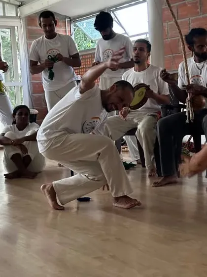 An instructor leads the game in the roda, playing the pandeiro (tambourine) to keep the rhythm. Music and movement are inseparable in Capoeira.