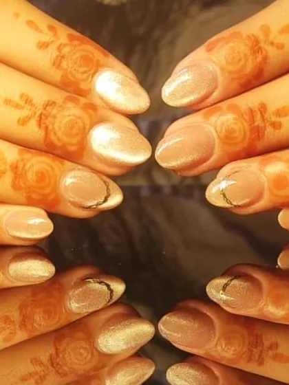 An elegant design perfect for a wedding guest or festive occasion, featuring shimmery nude nails with a delicate gold accent, paired with henna-adorned fingers.