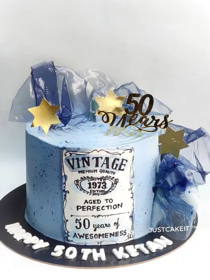 An abstract-style 50th birthday cake with a hand-painted vintage label. The design uses a cool blue palette and edible rice paper sails.