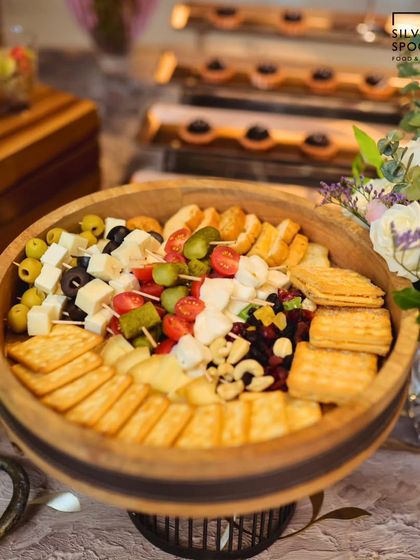 A large wooden bowl filled with a delightful mix of cheeses, crackers, olives, and nuts. This type of grazing bowl is perfect for encouraging guests to mingle and snack.