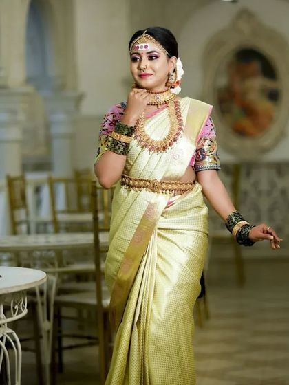 A bride in a beautiful off-white silk saree, adorned with our classic temple jewellery. The contrast of the pink blouse and gold jewellery is stunning.