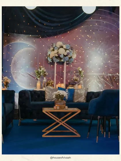 A cozy lounge setup with a celestial backdrop of a moon and stars. The deep blue velvet sofa and sequined cushions add to the luxurious, starry-night theme.