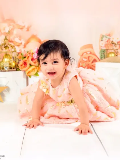 A crawling baby girl flashes a huge, happy smile in a lovely peach and pink floral setup. Her joy is contagious.