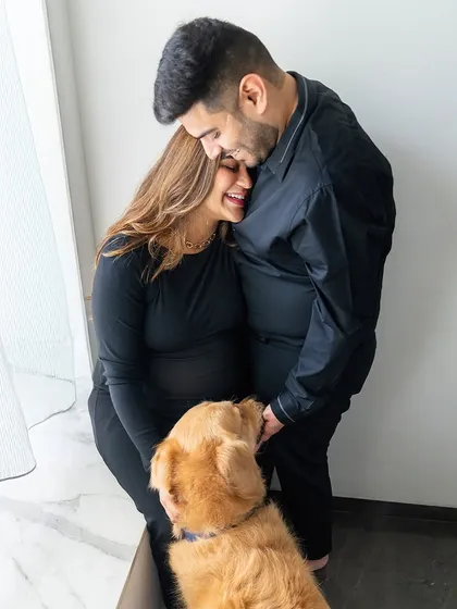 A candid moment of laughter and love. This photo captures the couple sharing a happy, intimate moment with their Golden Retriever, Hugo, during their black-and-white themed maternity shoot.