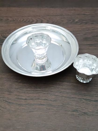 A simple pooja set with a plain German silver plate, a diya, and a small bowl.