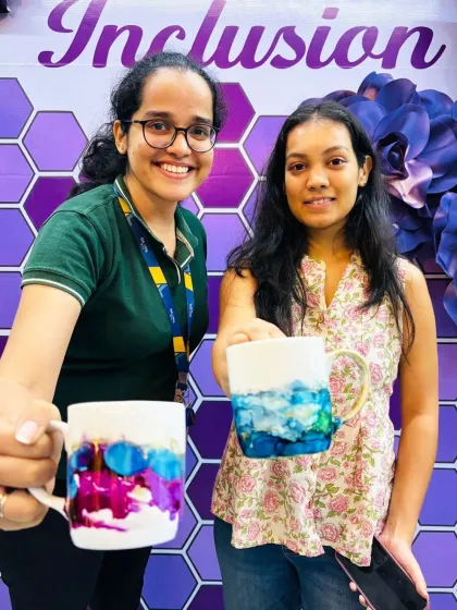 Two team members hold up their finished alcohol ink mugs, each a unique and vibrant design. It’s a great way to inspire inclusion and celebrate individual creativity.