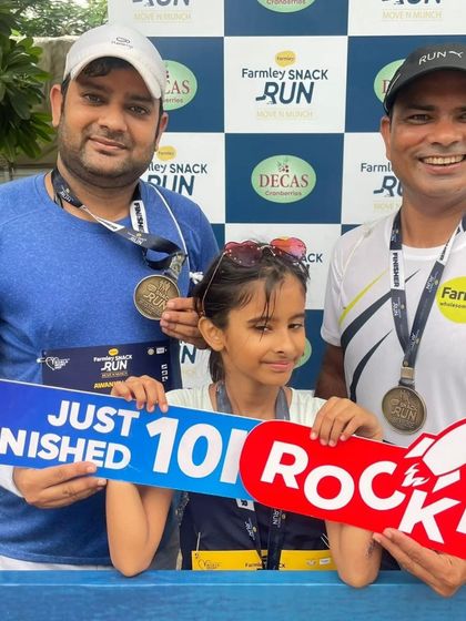 Two runners and a young participant proudly holding a 'Just Finished 10K Rocket' sign. Our events are family-friendly and inspiring for all ages.