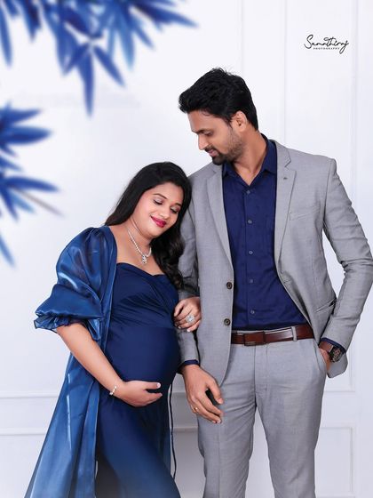 A loving couple portrait in a studio setting. The wife, in a beautiful blue gown, leans against her husband, creating a moment of quiet connection and support.