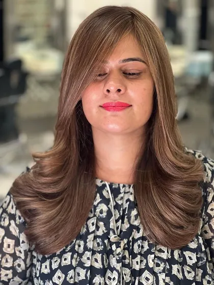 A close-up of a finished look featuring soft brown highlights and a layered haircut. The color placement is designed to complement the cut, making the layers and styling stand out.