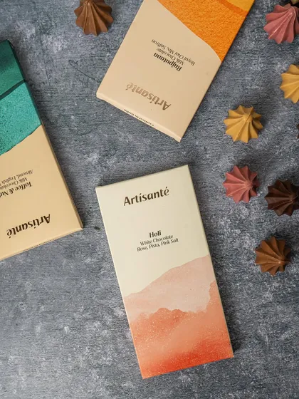 This flat lay photograph was for a Ganesh Chaturthi shoot, featuring artisanal chocolate bars and custom modak shaped chocolates. The textured grey background makes the warm colors of the packaging stand out.