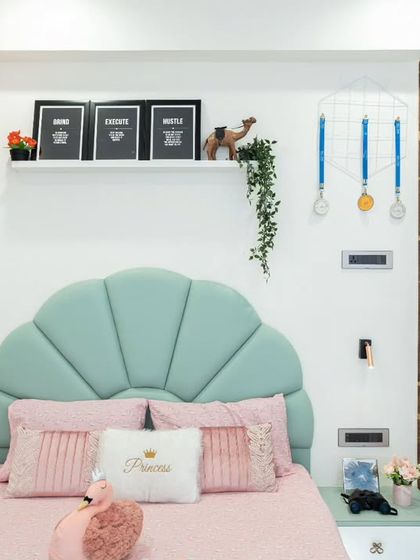 A close-up of the beautiful shell-shaped headboard in a mint green fabric, complemented by pink and white "Princess" cushions. The floating nightstand keeps the look clean and modern.