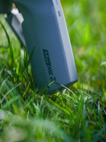 A product shot of the MOZA Mini MX2 gimbal in a natural, outdoor setting. This highlights the gear's portability and readiness for any adventure.