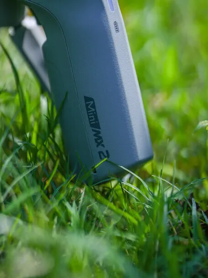 A product shot of the MOZA Mini MX2 gimbal in a natural, outdoor setting. This highlights the gear's portability and readiness for any adventure.