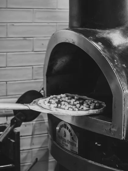 Where simplicity meets satisfaction. A pizza topped with cheese is placed into the hot wood-fired oven.